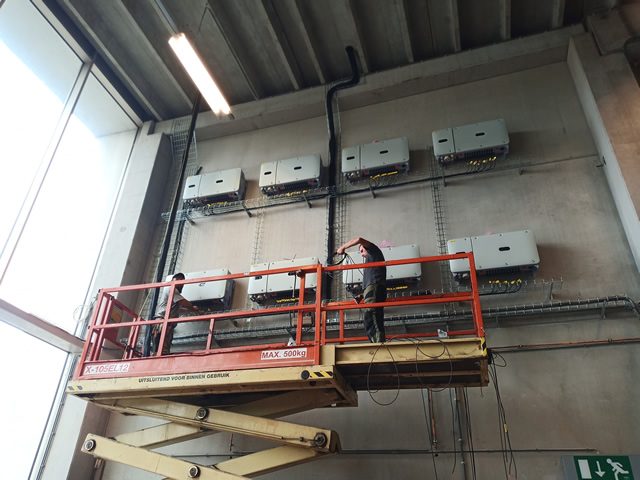 Hoogtewerker wekzaam aan omvormers zonnepanelen.